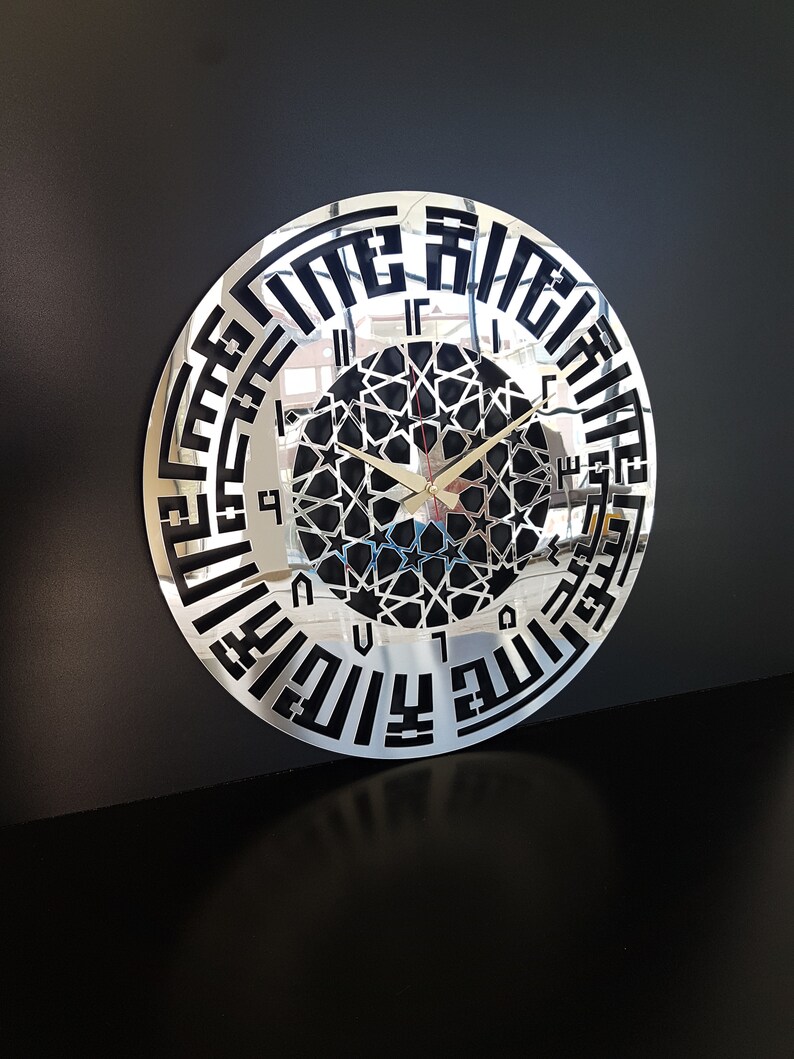May include: A silver mirrored wall clock with black Arabic numerals and a black geometric design in the center. The clock has a reflective surface.