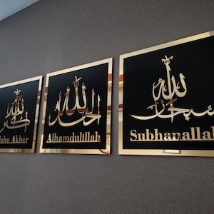 May include: Three square wall plaques with gold frames and black backgrounds. Each plaque features a different Arabic calligraphy inscription in gold. The inscriptions read "Allahu Akbar", "Alhamdulillah", and "Subhanallah".