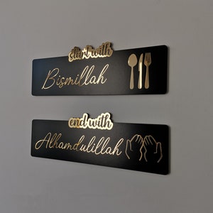 May include: Two black rectangular signs with gold lettering and icons. The top sign says "start with Bismillah" and has a gold fork, knife, and spoon. The bottom sign says "end with Alhamdulillah" and has two gold hands in a praying position.