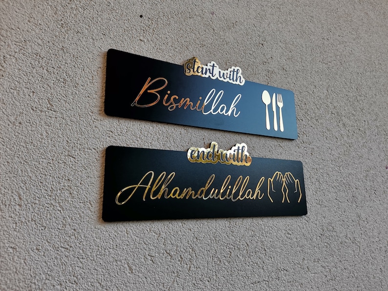 May include: Two black rectangular signs with gold lettering. The top sign says "Start with Bismillah" with a fork and spoon icon. The bottom sign says "End with Alhamdulillah" with two hands in a praying position.