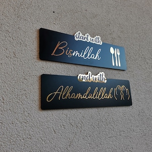 May include: Two black rectangular signs with gold lettering and icons. The top sign says "start with Bismillah" with a gold fork and spoon. The bottom sign says "end with Alhamdulillah" with two gold hands in a praying position.