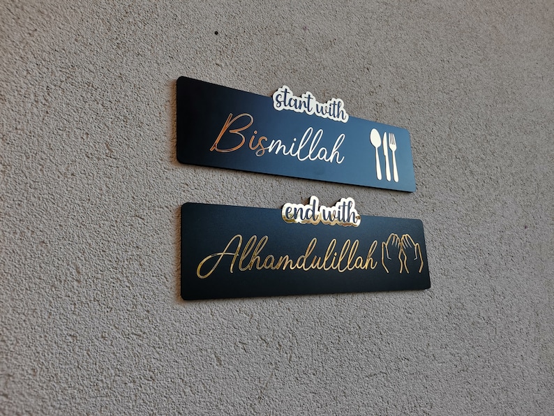 May include: Two black rectangular signs with gold lettering and icons. The top sign says "start with Bismillah" with a gold fork and spoon. The bottom sign says "end with Alhamdulillah" with two gold hands in a praying position.