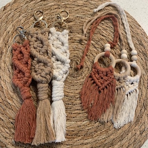 May include: Three macrame keychains with tassels in brown, beige, and white, and a macrame necklace with wooden rings and tassels in brown and beige.