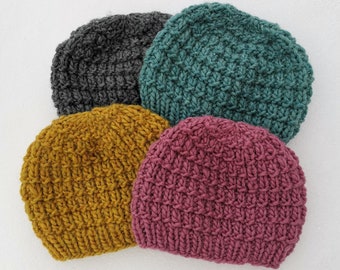 May include: Four knitted hats in different colors: gray, teal, mustard yellow, and pink. The hats are all made with a chunky yarn and have a simple, ribbed texture.