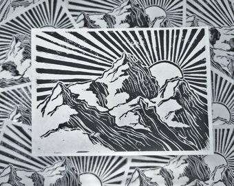 May include: Black and white linocut print of a mountain range with a sun rising behind it. The print has a stylized, graphic design.