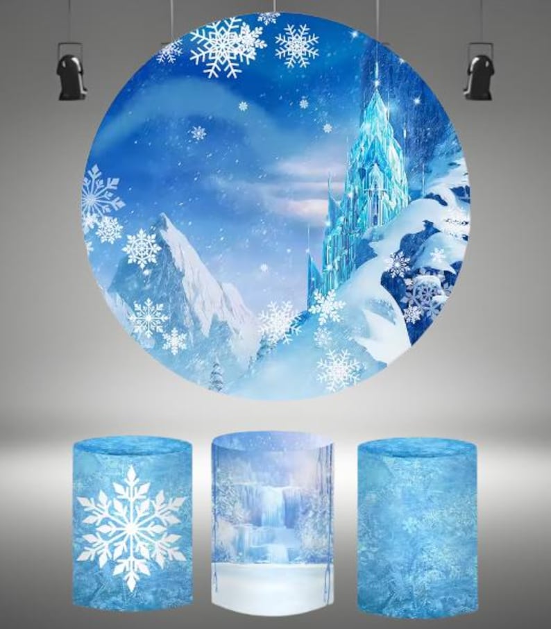 May include: A round backdrop with a blue and white winter scene featuring a tall ice castle and snow-covered mountains. The backdrop is surrounded by three blue and white cylindrical props with snowflake designs.