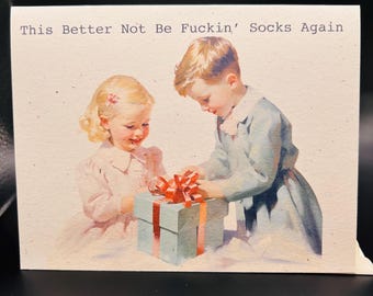May include: Greeting card with a vintage illustration of two children opening a gift. The gift is wrapped in blue paper with a red bow. The text on the card reads: "This Better Not Be Fuckin' Socks Again."