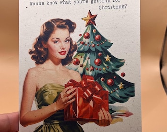 May include: A rectangular greeting card featuring a vintage-style illustration of a person in a green dress holding a red gift box in front of a decorated Christmas tree. The text at the top reads, Wanna know what you're getting for Christmas?