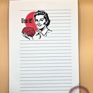 May include: A white rectangular sheet of lined stationery paper featuring a black and white illustration of a person holding a red brain. The text "Use it!" is printed in black next to the person. A circular logo is visible in the bottom corner.