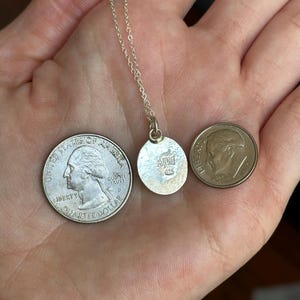 Pu&ograve; includere: Una collana d'argento con un piccolo ciondolo rotondo. Il ciondolo ha le iniziali "AJM" e "925". Una moneta da un quarto di dollaro e una da dieci centesimi sono accanto al ciondolo per il confronto delle dimensioni.