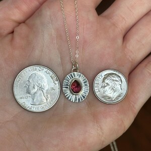 Pu&ograve; includere: Una collana con pendente in argento con una gemma rossa al centro. Il pendente &egrave; rotondo con un bordo strutturato. La collana &egrave; mostrata con un quarto di dollaro e una monetina da dieci centesimi per il confronto delle dimensioni.