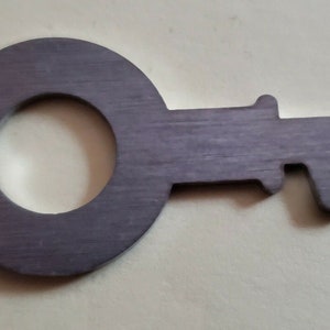 May include: A large, silver-colored metal key with a circular head and a detailed, intricate design. The key is made of a textured metal and has a slightly worn appearance.