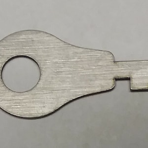 May include: A silver metal key with a round head and a single, small, serrated key bit.