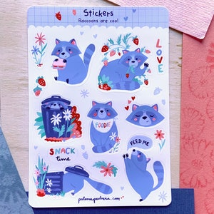 Może przedstawiać: Arkusz naklejek z ilustracjami niebieskich szopów praczy. Szopy są przedstawione z truskawkami i kwiatami, z tekstami takimi jak "Raccoons are cool", "Snack Time" i "Feed Me".