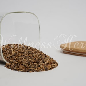 May include: A glass jar with a wooden lid, filled with dried, brown, and crumbly pieces of burdock root. The jar is tipped over, spilling the root onto a white surface.