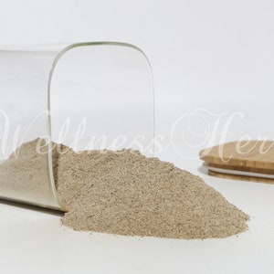 Puede incluir: Un tarro de vidrio con tapa de bambú, volcado, derramando un polvo marrón claro. El tarro es transparente y tiene forma cuadrada.