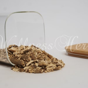 May include: A glass jar with a wooden lid filled with dried, light brown, chopped herbs. The jar is tipped over and the herbs are spilling out onto a white surface.