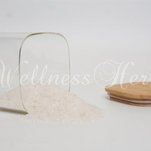 May include: A clear glass jar with a white lid is tipped over, spilling out white crystals. The lid is made of bamboo and has a white silicone seal.