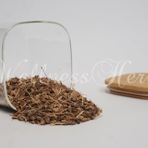 May include: A glass jar with a wooden lid, filled with dried herbs. The jar is tipped over, spilling the herbs onto a white surface. The jar has a square shape and the lid is a light brown color.
