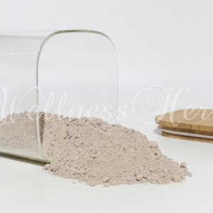 May include: A glass jar with a bamboo lid, tipped over, spilling out a light brown powder. The jar is clear and has a square shape. The lid is made of natural bamboo with a white silicone seal.