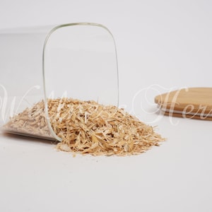 Puede incluir: Un tarro de vidrio con tapa de bambú, volcado, derramando hierbas secas desmenuzadas de color marrón claro.