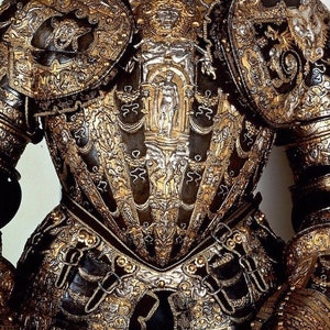 K&ouml;nnte beinhalten: Eine R&uuml;stung mit aufwendigen Gold- und Silberdetails. Die R&uuml;stung ist aus Metall und hat eine schwarze Basis. Die R&uuml;stung ist mit verschiedenen Mustern verziert, darunter florale Muster und Figuren.