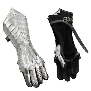 May include: A pair of silver metal gauntlets with a scale-like design. The gauntlets have a black leather strap with a buckle. The gauntlets are for the left and right hands.