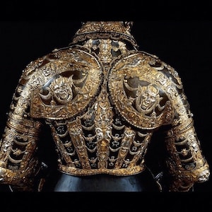 K&ouml;nnte beinhalten: Eine detailreiche, verzierte R&uuml;stung mit goldenen und silbernen Verzierungen. Die R&uuml;stung ist mit komplizierten Mustern und grotesken Gesichtern verziert.