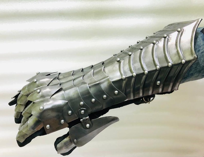 May include: A silver metal gauntlet with a scaly design and rivets. The gauntlet is made of metal plates that are connected by rivets. The gauntlet is designed to protect the hand and forearm.