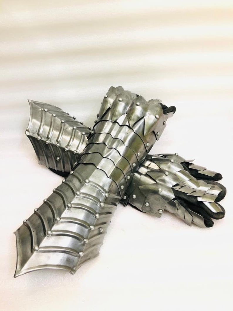 May include: A pair of silver metal gauntlets with a scaly design. The gauntlets are made of interlocking plates and have a pointed tip at the wrist.