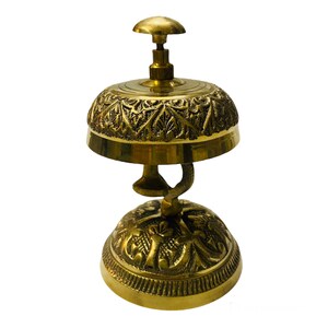 May include: A gold-toned brass hotel service bell with an ornate design. The bell has a rounded top and a base with intricate details.