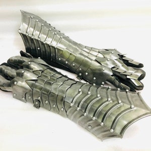 May include: A pair of silver metal gauntlets with a scaly design. The gauntlets are made of interlocking metal plates and have a pointed tip at the end.
