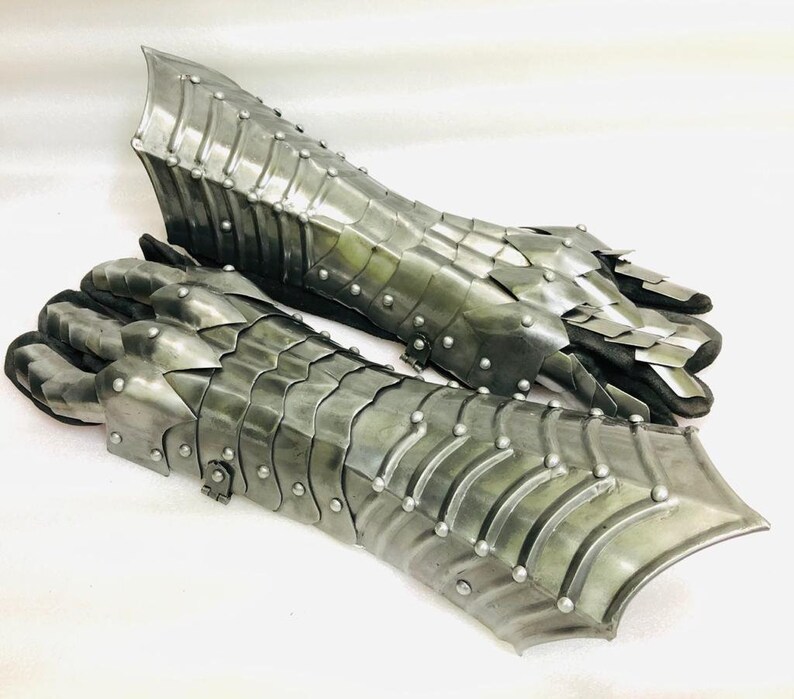 May include: A pair of silver metal gauntlets with a scaly design. The gauntlets are made of interlocking metal plates and have a pointed tip at the end.