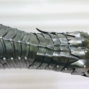 May include: A silver metal gauntlet with a spiked finger design. The gauntlet is made of overlapping plates and has rivets along the seams.