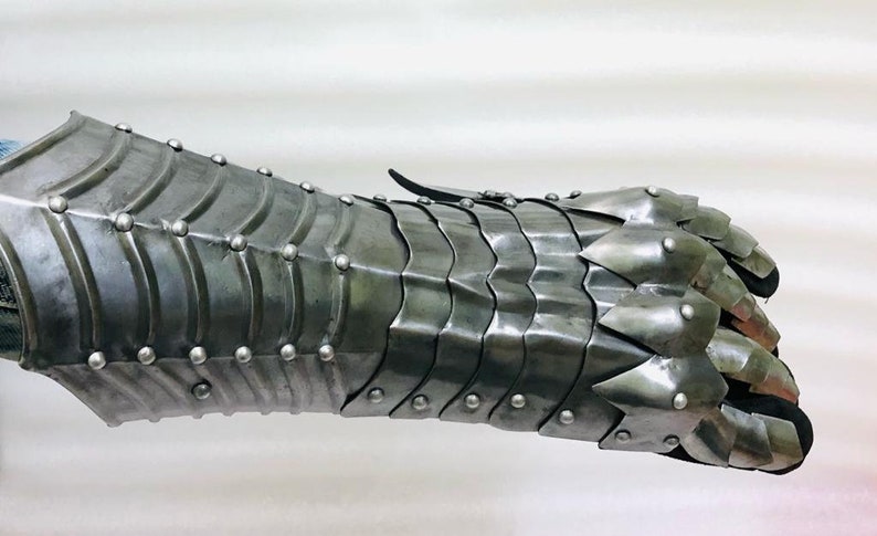 May include: A silver metal gauntlet with a spiked finger design. The gauntlet is made of overlapping plates and has rivets along the seams.