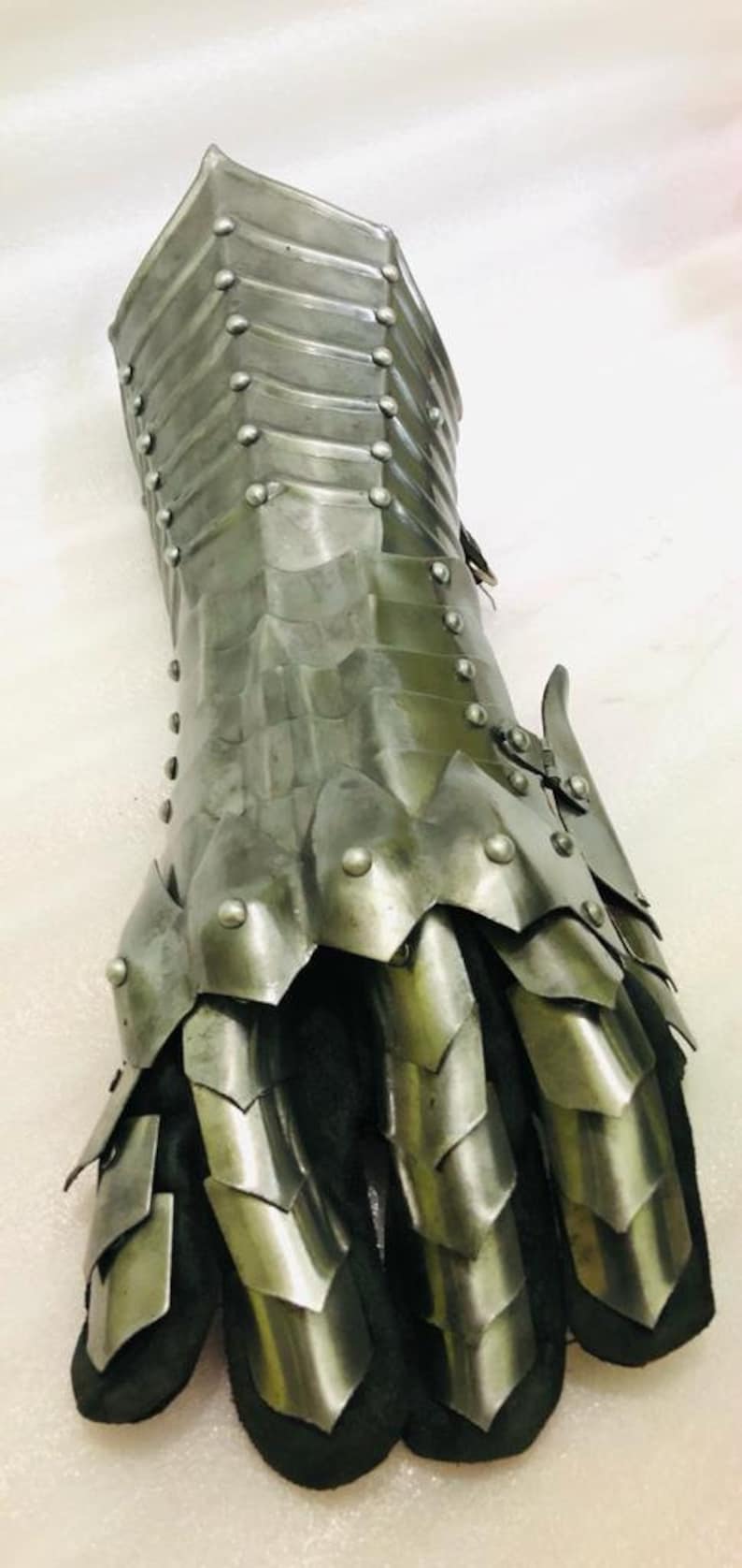 May include: A silver metal gauntlet with a segmented design and rivets. The gauntlet has a black leather lining and covers the entire hand and wrist.