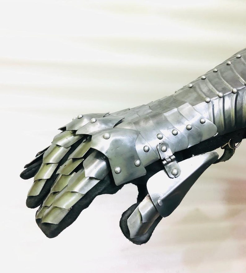 May include: A silver metal gauntlet with a segmented design and rivets. The gauntlet is made of multiple plates that are connected together. The gauntlet is designed to protect the hand and forearm.