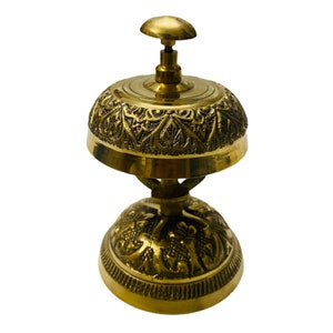 May include: A gold-toned brass hotel service bell with intricate floral designs. The bell has a round top and a base with a similar design.