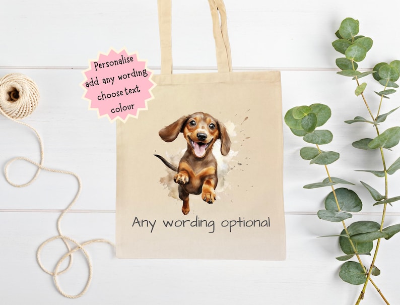 Peut inclure: Un sac fourre-tout en toile beige avec une illustration &agrave; l'aquarelle d'un chien teckel. Le chien est marron et beige avec la langue sortie. Le sac porte l'inscription "Any wording optional" et une &eacute;toile rose avec du texte.