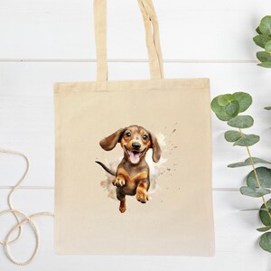 Peut inclure: Un sac fourre-tout en toile beige avec une illustration &agrave; l'aquarelle d'un chien teckel heureux. Le chien est marron et beige avec la langue sortie, semblant sauter hors d'une &eacute;claboussure de peinture. Le sac a deux anses beiges.