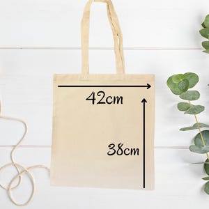以下が含まれることがあります： ベージュのキャンバス地のトートバッグで、黒い文字で「42cm」と「38cm」と書いてあり、バッグのサイズを示しています。