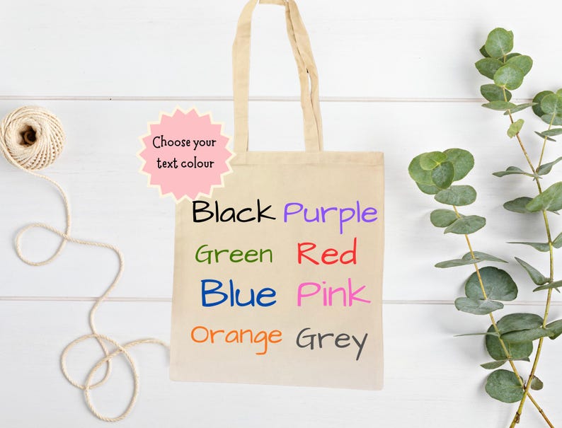 Peut inclure: Un sac fourre-tout en toile beige avec diff&eacute;rentes options de couleurs de texte : noir, violet, vert, rouge, bleu, rose, orange et gris. Le sac a une poign&eacute;e beige clair et le texte "Choose your text colour" dans un cartouche rose.