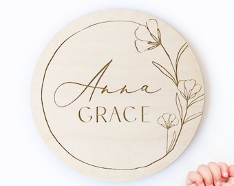 Peut inclure: Une pancarte ronde en bois avec un motif floral et le nom "Anna Grace" gravé en lettres dorées.
