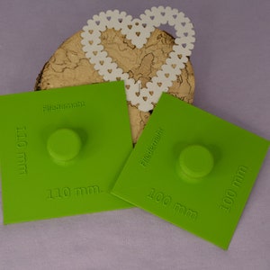 Può includere: Due cerchi di plastica verde con il testo "Filledermahlk" e misure di 110 mm e 100 mm. I cerchi sono su una superficie di legno con un cuore di carta bianca.