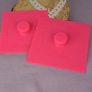 May include: Two pink plastic circle templates for crafting. The larger template is 115 mm in diameter and the smaller template is 105 mm in diameter. The templates are labeled "Filecormant".