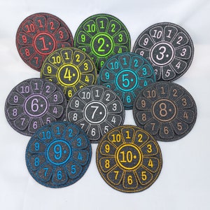 Peut inclure: Dix cercles en feutre colorés avec les chiffres de 1 à 10, chacun avec un motif de fleur et une bordure noire cousue.