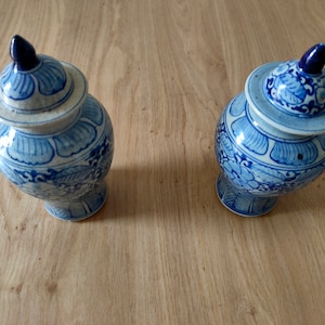 Op de afbeelding: Twee blauwe en witte porseleinen potten met deksel met bloemmotieven. De potten staan op een houten oppervlak.
