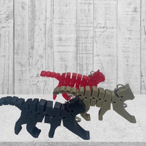 Puede incluir: Tres llaveros articulados con forma de gato, en negro, verde y rojo. Los llaveros son de plástico y tienen un diseño segmentado.