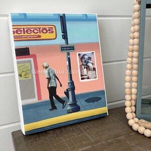 May include: A canvas print depicting a street scene with a person walking with an umbrella. The artwork features a pink building, a street sign that reads "PARADA 15", and a sign that says "SELECIOS".