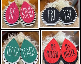 May include: Four pairs of layered faux leather earrings. Top left: pink teardrops with white text BE KIND over black and white stripes. Top right: black circles with white text FRI YAY over stripes. Bottom left: green teardrops with white text TEACH over polka dots. Bottom right: red teardrops with black text MS MILLER over black glitter.